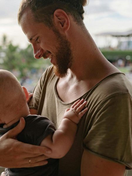 A bearded father holds his baby, sharing a tender moment outdoors.