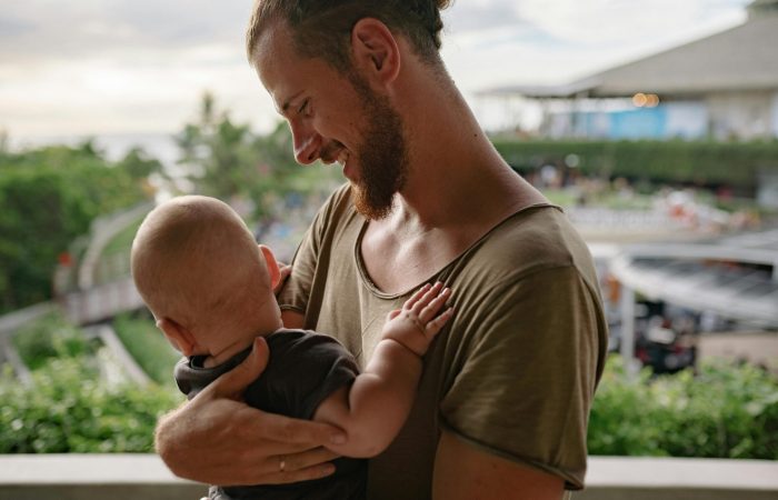 A bearded father holds his baby, sharing a tender moment outdoors.